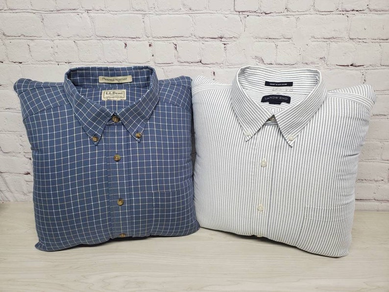 May include: Two button-down shirts, one blue plaid and one white with thin gray stripes. Both shirts are folded and arranged as pillows.