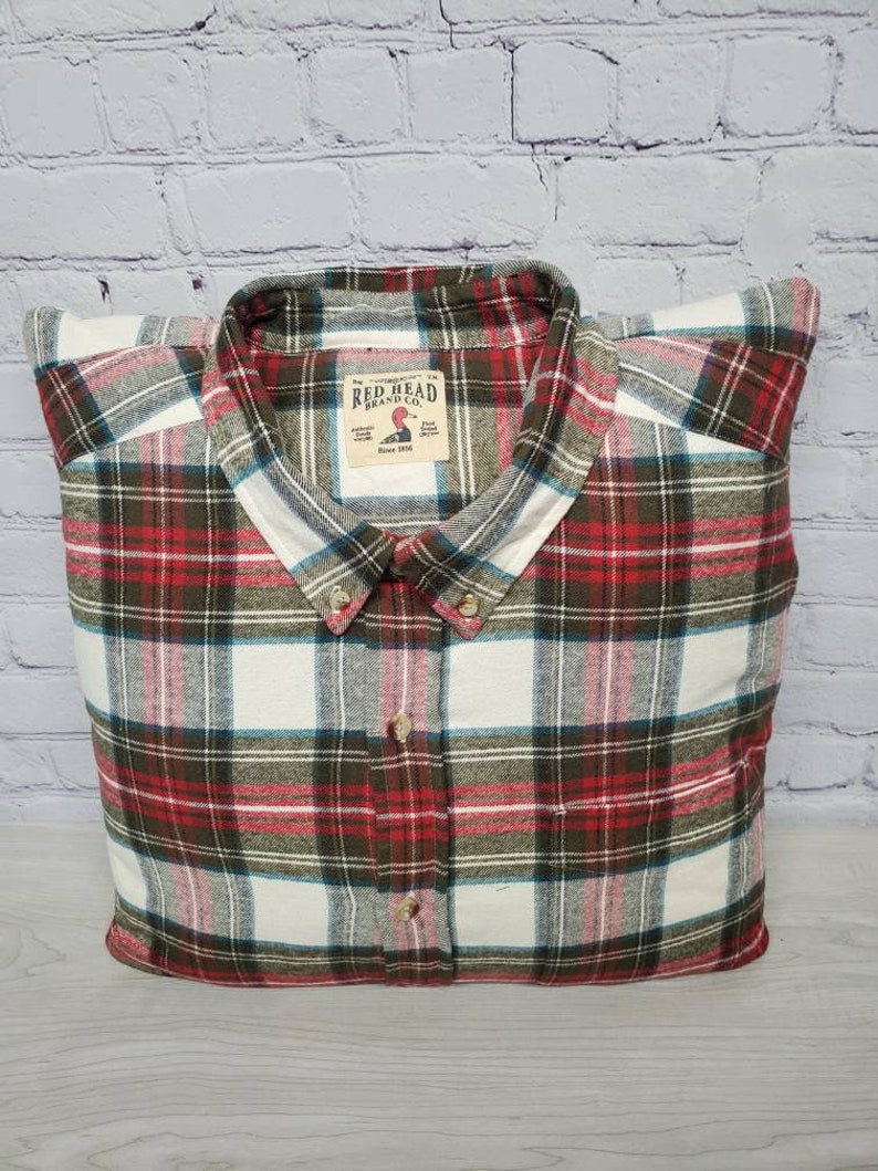 May include: A red, white, and green plaid flannel shirt with a Red Head Brand Co. label. The label has a red duck logo and the text "Since 1911".