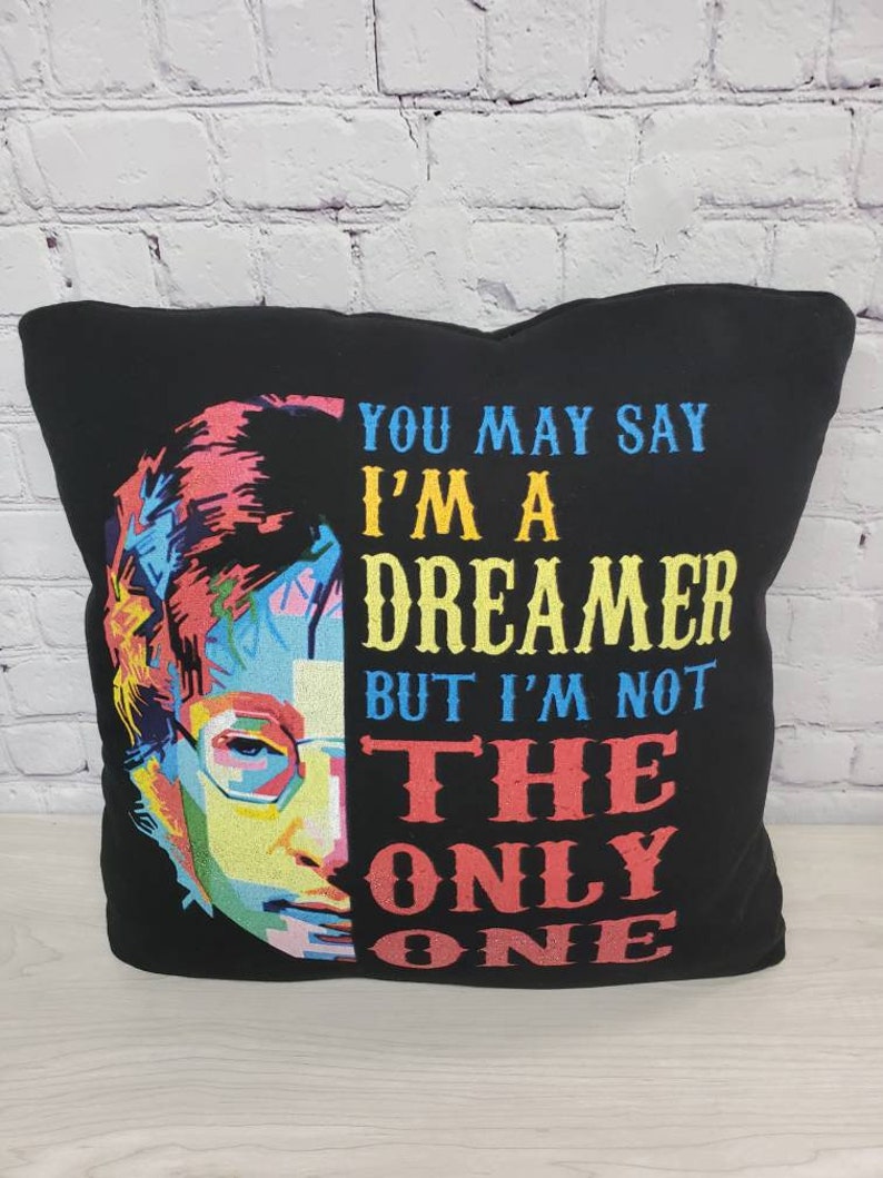 May include: Black pillow with a colorful pop art image of John Lennon and the text "You may say I'm a dreamer but I'm not the only one."