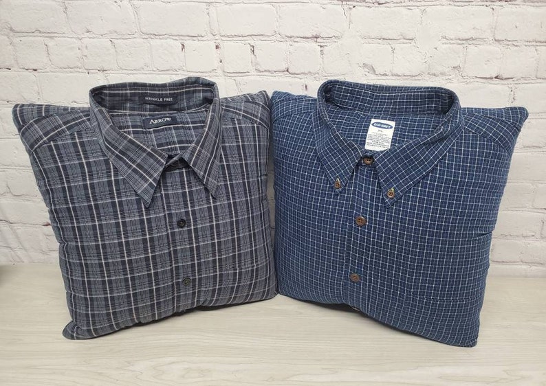 May include: Two plaid pillow covers made from repurposed shirts. The pillow on the left is gray and black with the text "Wrinkle Free" and "Arrow" on the collar. The pillow on the right is blue and white with the text "Old Navy" on the collar.
