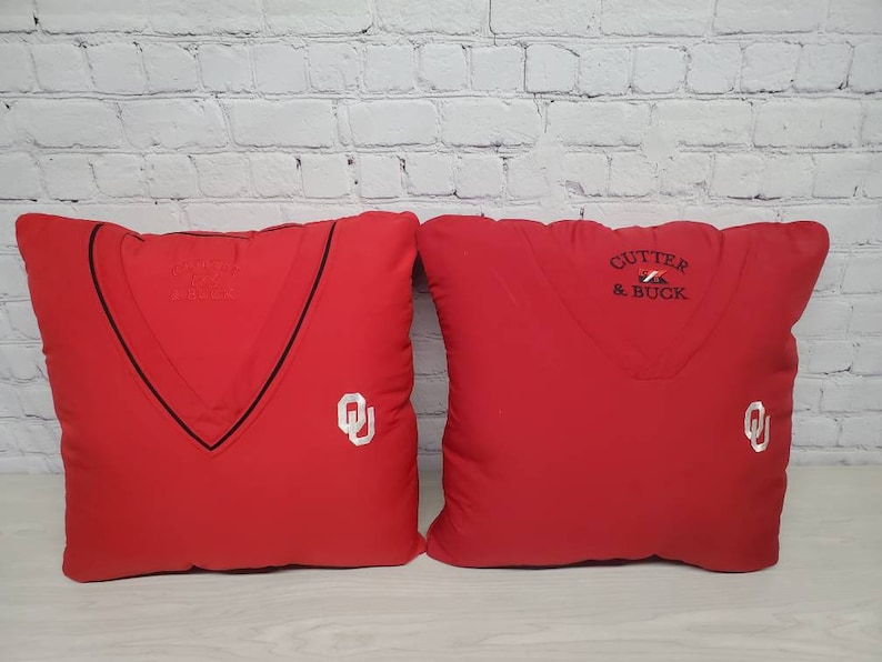 May include: Two red throw pillows with white embroidered logos. One pillow has the text "CUTTER & BUCK" and the other has a stylized "OU" logo.