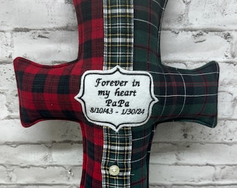 May include: A red and green plaid cross-shaped pillow with a white embroidered patch that reads "Forever in my heart Papa 8/10/43 - 1/30/24".