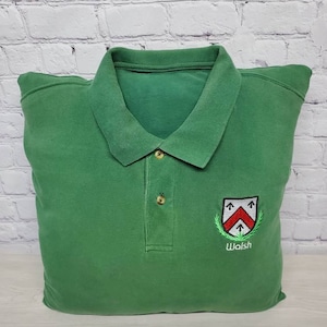 May include: Green polo shirt with a white embroidered crest and the word "Walsh" underneath.