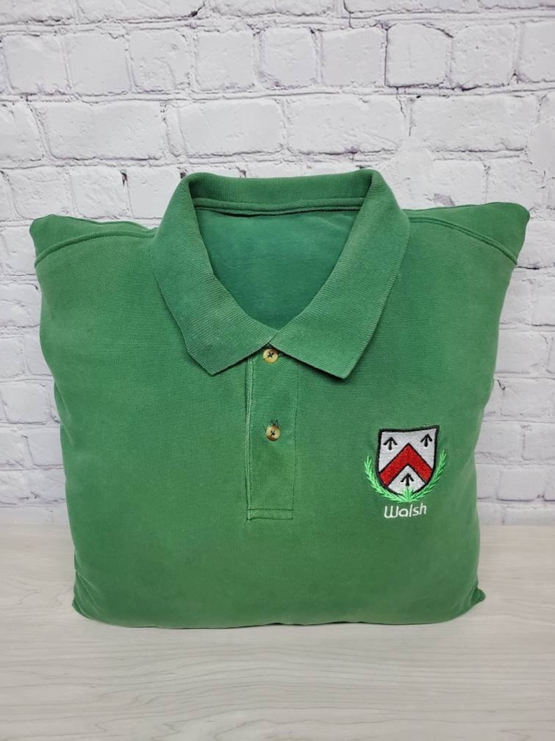 May include: Green polo shirt with a white embroidered crest and the word "Walsh" underneath.