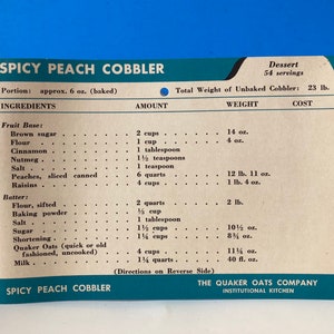 May include: A vintage recipe card for Spicy Peach Cobbler, featuring a list of ingredients and measurements in ounces and quarts. The card is printed on white paper with blue text and a blue border. The card is from The Quaker Oats Company Institutional Kitchen.