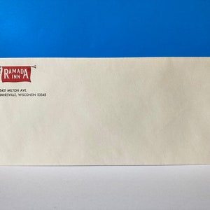 May include: A white envelope with a red and white Ramada Inn logo featuring a cartoon man holding a trumpet. The address 3431 Milton Ave. Janesville, Wisconsin 53545 is printed below the logo.