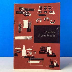 May include: A red and black cookbook cover with the title "A primer of yeast breads". The cover features illustrations of bread, dough, and baking tools.
