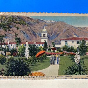 May include: Vintage postcard featuring the El Mirador Hotel in Palm Springs, California, with a mountain backdrop. The image shows a white building with a bell tower, lush gardens, and people walking on a path. The text reads "Gardens, El Mirador Hotel, Palm Springs, California, now Torney General Hospital."