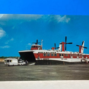 Puede incluir: Un aerodeslizador rojo y blanco con el nombre "Hoverlloyd Swift" y el número de matrícula "GH-2004" impreso en el lateral. El aerodeslizador está atracado en un puerto y una furgoneta blanca y un coche se dirigen hacia él.