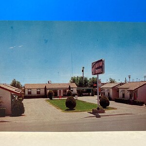 Pode incluir: Um cartão postal vintage mostrando um motel com uma placa que diz "The Blue Inn Motel". O motel é um edifício de um andar com telhado vermelho e paredes brancas. Há várias árvores e arbustos na frente do motel.
