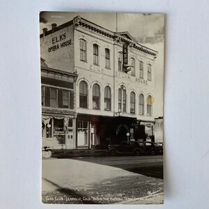 Puede incluir: Una fotografía en blanco y negro del Elks Opera House en Leadville, Colorado. El edificio tiene un gran letrero que dice "Elks Opera House". Hay un coche estacionado frente al edificio.