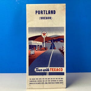 May include: A vintage Texaco map for Portland, Oregon. The map features a red star with a white circle and the text "Tour with Texaco". The map is illustrated with a Texaco gas station and a road.