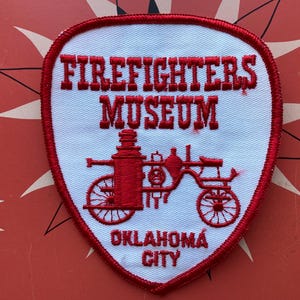 May include: White patch with red embroidered text "Firefighters Museum Oklahoma City" and a red illustration of a vintage fire engine.