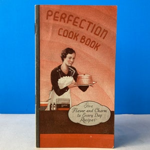 Pode incluir: Um livro de receitas vintage intitulado "Perfection Cook Book" com uma mulher segurando um bolo e o texto "Give Flavor and Charm to Every Day Recipes".