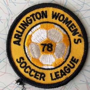 May include: A yellow and black embroidered patch with the text "Arlington Women's Soccer League" and the number "78" inside a white soccer ball.