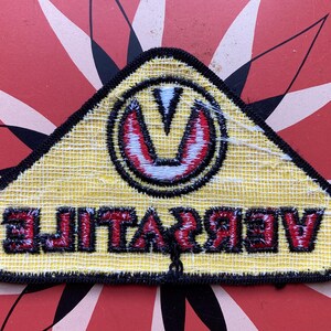 May include: Yellow triangular patch with black stitching and a red and white stylized "V" logo. The text "VIBRATE" is written in red letters below the logo.