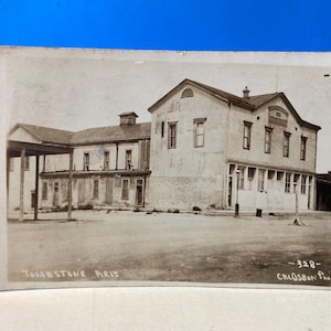 May include: Vintage black and white postcard featuring the Old Fellow Building in Tombstone, Arizona. The postcard shows a two-story building with a covered porch and several windows. The text "Tombstone Ariz" is visible.