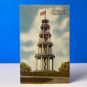 Può includere: Una cartolina vintage con una foto di una torre di osservazione a cinque piani con una scala a chiocciola. La torre è sormontata da una bandiera americana e si trova nel Vicksburg National Military Park, Mississippi. Il testo sulla cartolina recita "Observation Tower on Jackson Road National Military Park Vicksburg, Miss. - 6"