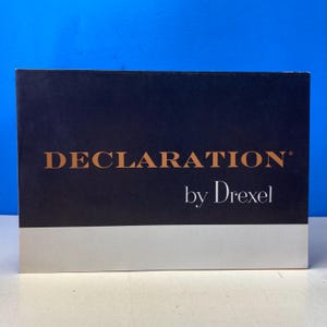 May include: A rectangular box with a navy blue upper section and a light gray lower section. The text "DECLARATION" in gold lettering is above "by Drexel" in white lettering.