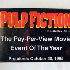May include: A black and red button with the text "PULP FICTION" in red letters with a yellow outline. The text "The Pay-Per-View Movie Event Of The Year" is in white letters on a black background. The text "Premieres October 20, 1995" is in white letters on a black background. The text "MIRAMAX FILMS" is in white letters on a black background.
