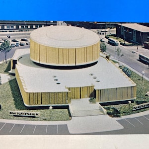 May include: A vintage postcard depicting the Dow Planetarium, a mid-century modern building with a circular roof and a rectangular base. The postcard shows the building in a detailed architectural style, with the text "DOW PLANETARIUM".