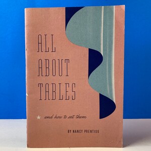 Peut inclure: Un livre rose intitulé "ALL ABOUT TABLES and how to set them" par Nancy Prentiss. La couverture présente un motif abstrait bleu et vert.