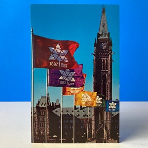 May include: A postcard depicting the Peace Tower of the Canadian Parliament Buildings in Ottawa, Ontario, Canada. The tower is flying flags commemorating Canada's centenary in 1967. The flags are red, purple, yellow, and green with a white star and the text "1867 1967".