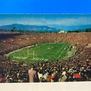 May include: Vintage postcard featuring a full stadium during a football game. The green field has white yard lines and goalposts. The stands are packed with spectators. Mountains are visible in the background.