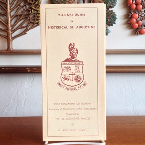 May include: A vintage visitors guide to historical St. Augustine, Florida. The cover features a red and white crest with a knight in armour and the text "400th Anniversary" and "St. Augustine, Fla. 1565". The guide is presented by the St. Augustine Jaycees.