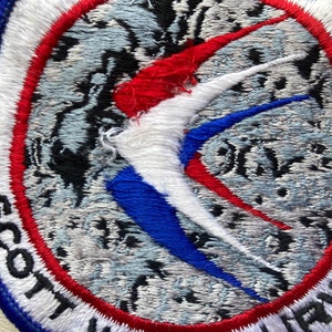 Peut inclure: Un &eacute;cusson brod&eacute; blanc, rouge et bleu avec le texte "Scott Air Force Base" en lettres noires.