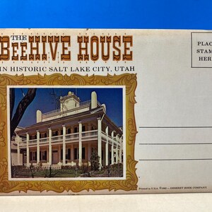 Op de afbeelding: Vintage ansichtkaart met The Beehive House in Historic Salt Lake City, Utah. De ansichtkaart heeft een gouden, sierlijke lijst rond een kleurenfoto van het huis. De tekst "PLACE STAMP HERE" staat in de rechterbovenhoek.