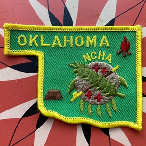 May include: A green and yellow embroidered patch shaped like the state of Oklahoma. The patch features the words "OKLAHOMA" and "NCHA" along with a Native American design.