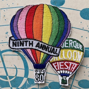 May include: Embroidered patches featuring hot air balloons. One patch reads "NINTH ANNUAL" on a banner. The other patch says "ALBUQUERQUE BALLOON FIESTA". The balloons are in rainbow colors.