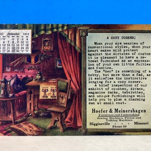 May include: A vintage postcard depicting a cozy living room interior with a calendar for November 1911. The room features a couch, a table, a chair, and a rug. The text on the postcard reads "A Cozy Corner!" and includes a description of the benefits of having a cozy corner in your home. The postcard is advertising the services of Hoefer & Meinershagen, a furniture and undertaking business in Higginsville, Missouri.