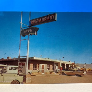 May include: A vintage postcard showing a roadside restaurant with a neon sign that reads "Restaurant". The sign is attached to a pole with a neon arrow pointing to the right that reads "Open". There are cars parked in front of the restaurant, and the sky is blue.