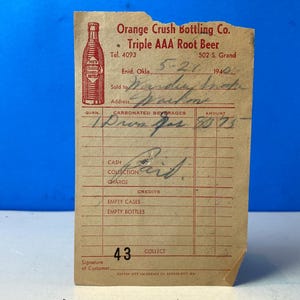 May include: Vintage Orange Crush Bottling Co. receipt from 1940. The receipt is tan with red text and a red illustration of an Orange Crush bottle. The receipt includes handwritten details and the text "Triple AAA Root Beer."