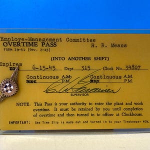 May include: A yellow overtime pass card with the text "Employe-Management Committee Overtime Pass Form 28-51 (Rev. 2-43) R. B. Means (INTO ANOTHER SHIFT)" and "Expires 6-15-45 Dept. 315 Clock No. 34807 Continuous A.M. P.M. Continuous A.M. P.M.". The card has a handwritten signature and the text "NOTE: This Pass is your authority to enter the plant and work overtime. It must be retained by you until completion of overtime and then turned in to officer at Clockhouse. IMPORTANT: See Time Slip is made out and turned in to your Timekeeper NOW."