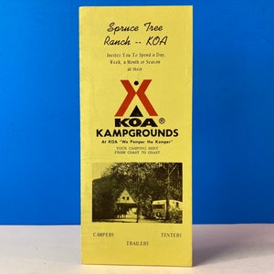 May include: A yellow brochure for Spruce Tree Ranch KOA Kampgrounds. The brochure features a red and white KOA logo and a photo of a wooded area with a cabin and a camper.