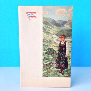 May include: A vintage postcard featuring a woman in traditional Norwegian clothing standing on a hill overlooking a valley. The postcard has the text "N.A.L" and "WALLINDAL" printed on it.