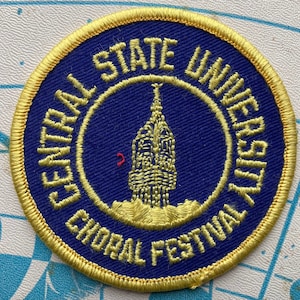 May include: A gold embroidered patch with the text "Central State University Choral Festival" around a blue circle with a gold building in the center.