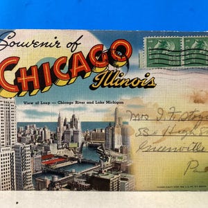 May include: Vintage postcard featuring a cityscape of Chicago, Illinois, with the words "Souvenir of Chicago Illinois" in bold lettering. The postcard includes a view of the Loop, Chicago River, and Lake Michigan.
