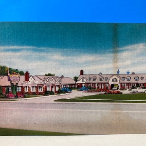 May include: Vintage postcard featuring the Colonial Manor, a motel with a red brick facade and a sign. The image shows a long, low building with multiple rooms, a driveway, and a well-manicured lawn. The sky is blue with a few clouds.