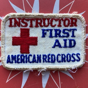 May include: White patch with red embroidered cross and blue embroidered text "Instructor First Aid American Red Cross"