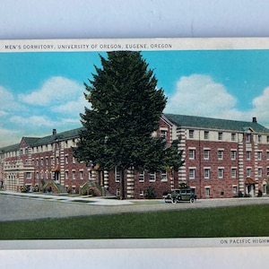 May include: A vintage postcard depicting a brick building with white trim. The building is labeled "Men's Dormitory, University of Oregon, Eugene, Oregon". A large evergreen tree stands in front of the building. The postcard is labeled "On Pacific Highway".