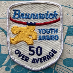 Può includere: Toppa bianca con testo ricamato in blu "Brunswick Youth Award" e una figura gialla che fa bowling. Sotto la figura, testo blu "Over 50 Average".