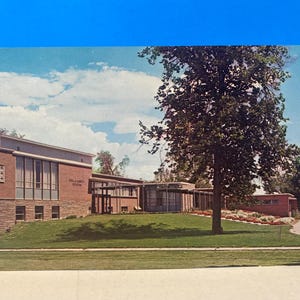May include: A vintage postcard featuring a brick building with a large window and the text "Fine Arts Studio" above it. The building is surrounded by a grassy lawn and a large tree.