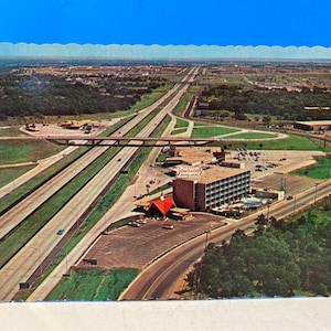 May include: An aerial view of a motel with a red roof and the words "Johnson's Motel" on the side. The motel is located near a highway with several cars driving on it. The image is a vintage postcard.