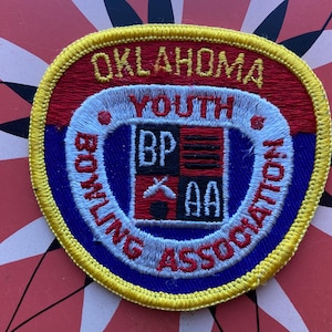 May include: A yellow, blue, red, and white embroidered patch with the text "Oklahoma Youth Bowling Association" and a logo with the letters "BP" and "AA" inside a shield.