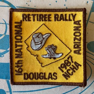 May include: Yellow embroidered patch with brown trim featuring text: "RETIREE RALLY", "16th NATIONAL", "ARIZONA", "DOUGLAS", "1987 NCHA". A light blue cowboy hat and boot are inside a yellow Arizona outline.