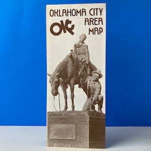 Puede incluir: Un mapa vintage del área de Oklahoma City con una foto en blanco y negro de una estatua de bronce de dos hombres a caballo. La estatua está sobre un pedestal con el año 1889 inscrito en él. El texto "Oklahoma City Area Map" está impreso en negro en la parte superior del mapa.